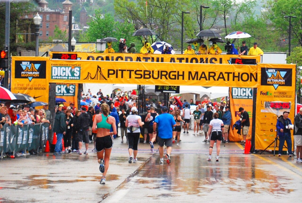 Runners approaching the Pittsburgh Marathon finish line under a yellow banner